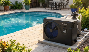 A black TURBRO pool heat pump and filtration system installed on a paved patio next to a clear blue swimming pool in a backyard.